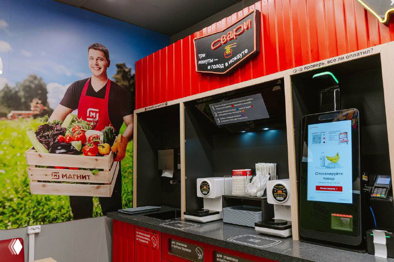 Уголок с оборудованием и раменоваркой в фирменной зоне «Магнит»: панель управления аппарата и рекламный визуал на стене.