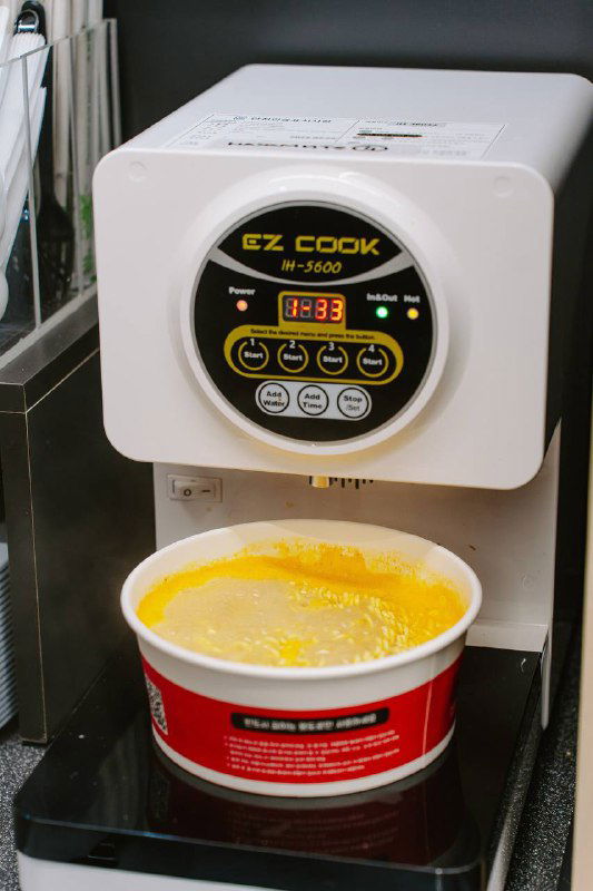 Крупный план раменоварки EZ COOK во время приготовления порции: чашка с продуктом и управляющая панель с индикатором температуры.