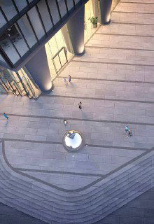 Площадка перед входом и тротуар с декоративными элементами: панорамный вид сверху на зону доступа к деловому центру и небольшие группы людей.