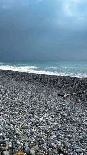 Каменистый пляж под хмурым небом и штормовое море на горизонте, изображение передаёт атмосферу волнения, одиночества и эмоционального шторма.