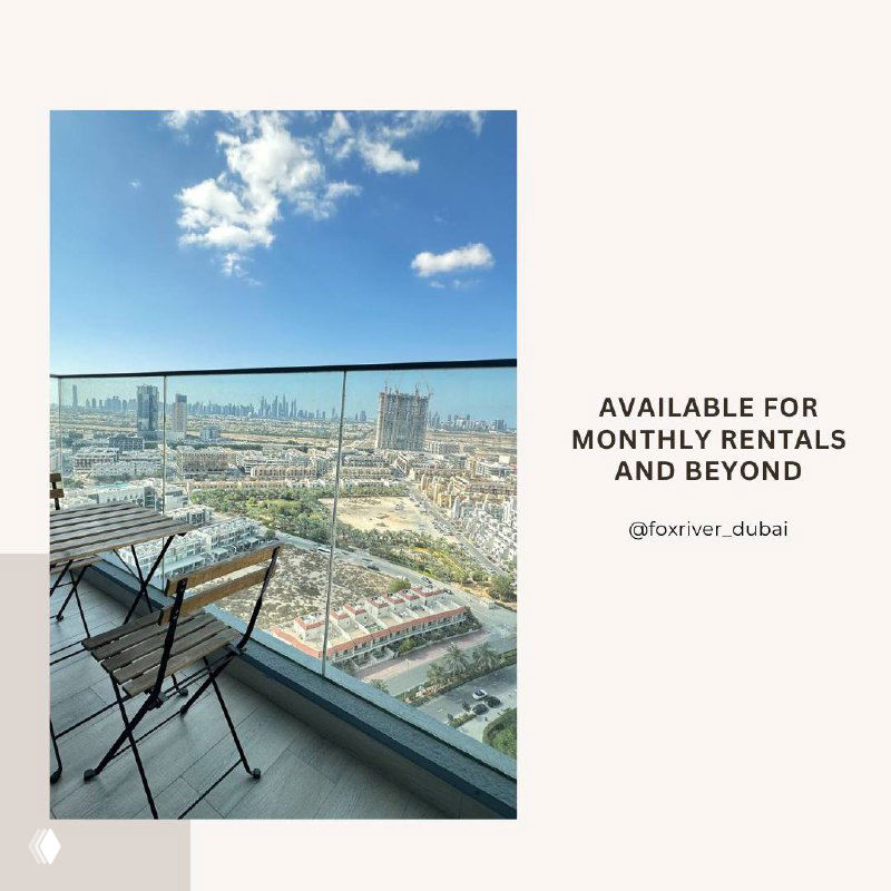 Balcony view from the studio apartment in Dubai with outdoor chairs and a wide panorama of the city skyline and blue sky.