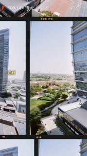 View from a high-rise in Dubai through window frames: modern glass towers, landscaped park and low-rise buildings under a clear sky.