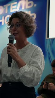 Ангелина Самадова выступает с микрофоном на профессиональной конференции по гостиничному бизнесу; видно полурост, фон с элементами брендирования мероприятия.