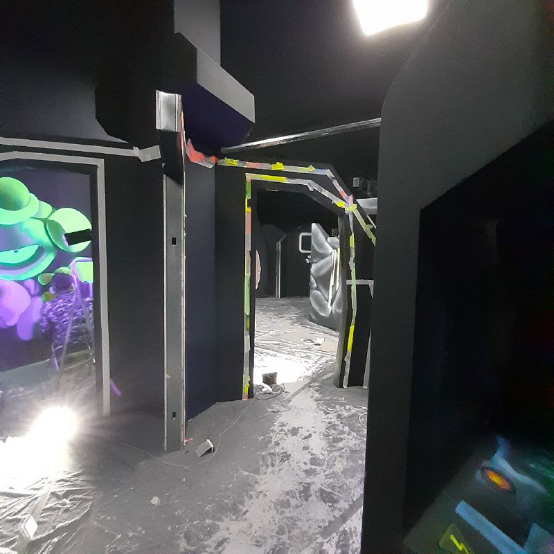 Коридор игровой зоны с чёрными стенами и частично нанесённой флуоресцентной раскраской — процесс оформления проходов и декораций.