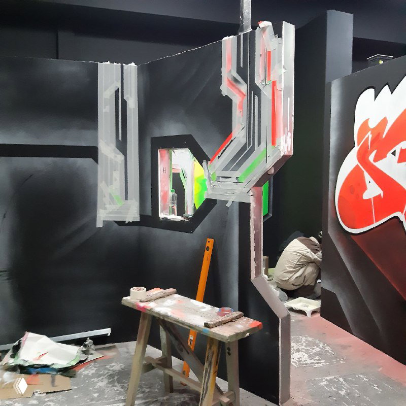 Рабочее место: столик с красками и инструментами на фоне чёрных стен и отчасти готовой графики, вид процесса оформления интерьера.