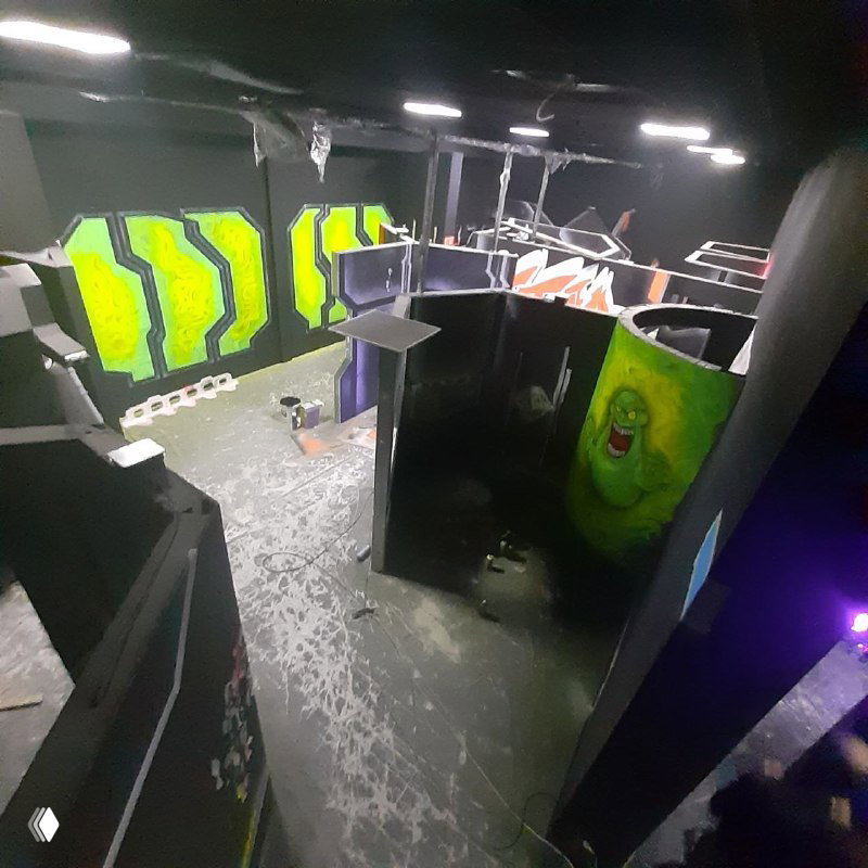 Общий вид игровой зоны сверху: разделённая на секции арена с яркими флуоресцентными панелями и переходами между зонами для лазер-тага.