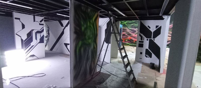 Рабочая сцена: лестница, светильники и инструменты на фоне нескольких оформленных панелей с чёткой контрастной росписью.