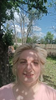 Портрет женщины на открытом воздухе под деревом, солнечные блики на лице, на заднем плане забор и зелёный сад.