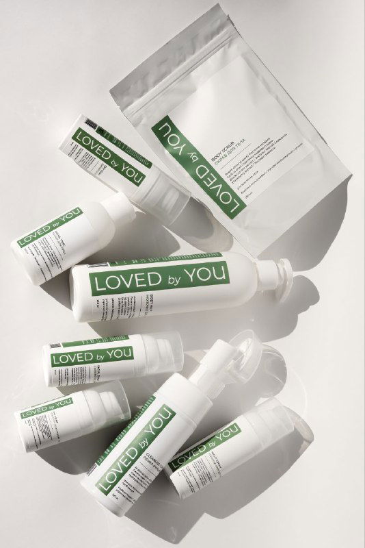 Несколько флаконов и пакетиков Loved by You на светлом фоне, размещённые в ряд; видно этикетки бренда и простую упаковку.