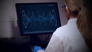 Лаборант в белом халате за компьютером анализирует данные и графики — иллюстрация научного подхода к разработке косметических формул.