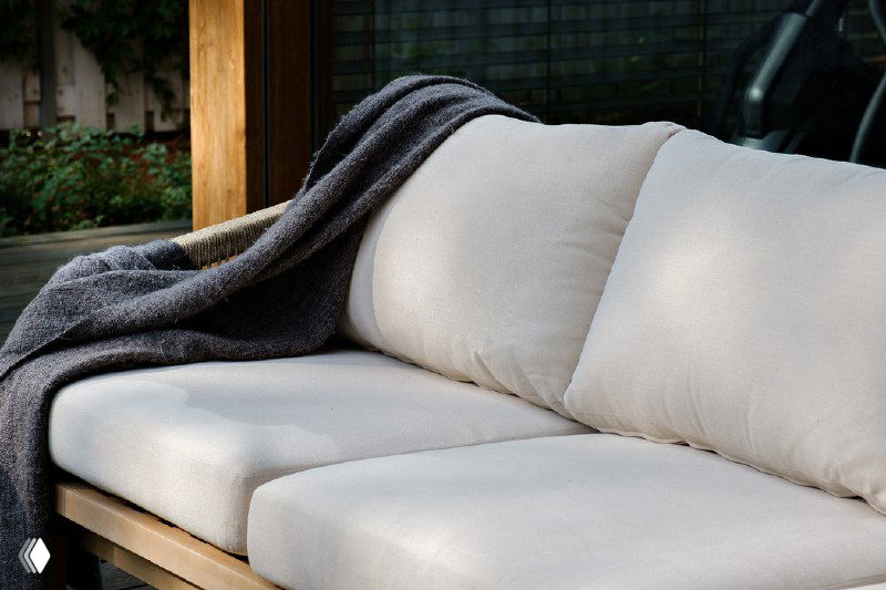 Крупный план мягких сидений дивана RIMINI с бежевыми чехлами и тёмным пледом, акцент на комфорт и текстуру материалов.