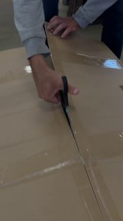 Руки человека, режущие упаковочный картон ножницами при распаковке или подготовке деталей мебельного комплекта к сборке в магазине