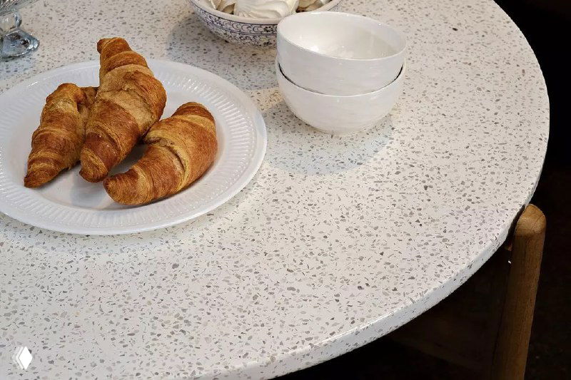 Крупный план текстуры столешницы круглого стола TALARA с тарелкой и круассанами — сочетание прочного покрытия и эстетики для семьи.