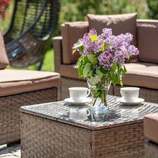 Крупный план стеклянного столика из плетёного ротанга с вазой сирени и двумя чашками — деталь комплекта, создающая уютную атмосферу