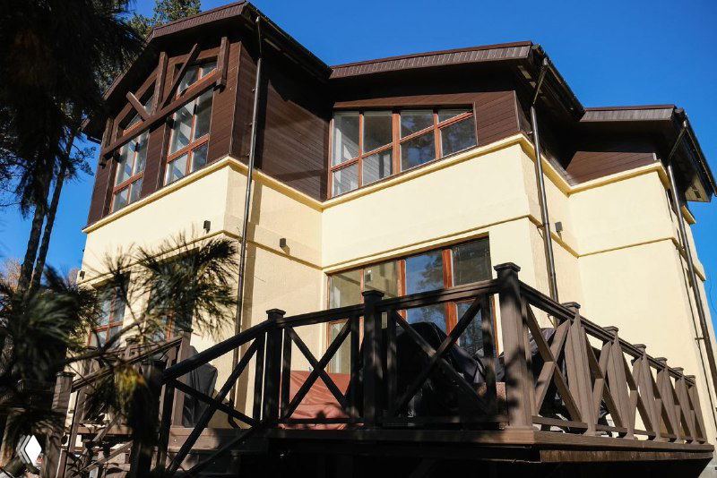 Вид на дом и террасу с балюстрадой из ДПК в солнечный осенний день, заметны ограждение и фасад коттеджа.