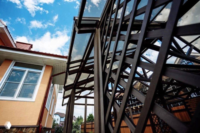 Конструкция перголы с крупным планом опорных балок и соединений; профиль и монтажные элементы на фоне фасада дома, материал — ДПК.