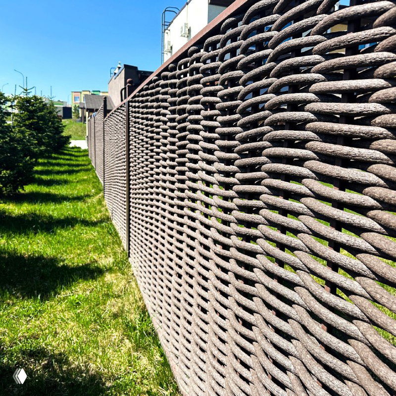 Крупный план плетёной структуры полимерной лозы на секции забора; видна текстура и переплетения материала под солнечным светом.