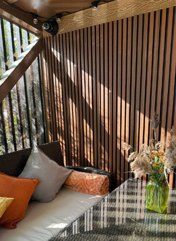 Уличная или верандная зона с вертикальными ДПК-ламелями, мягкая мебель и солнечные блики — пример фасадно-интерьерного применения.