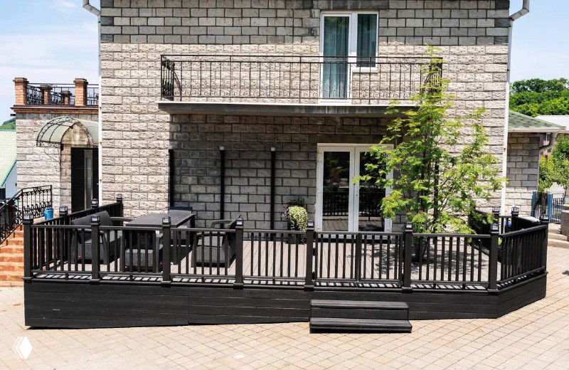 Днём снимок просторной террасы с высокими ограждениями и чёрной доской ДПК Polivan на фоне светлого каменного фасада дома.