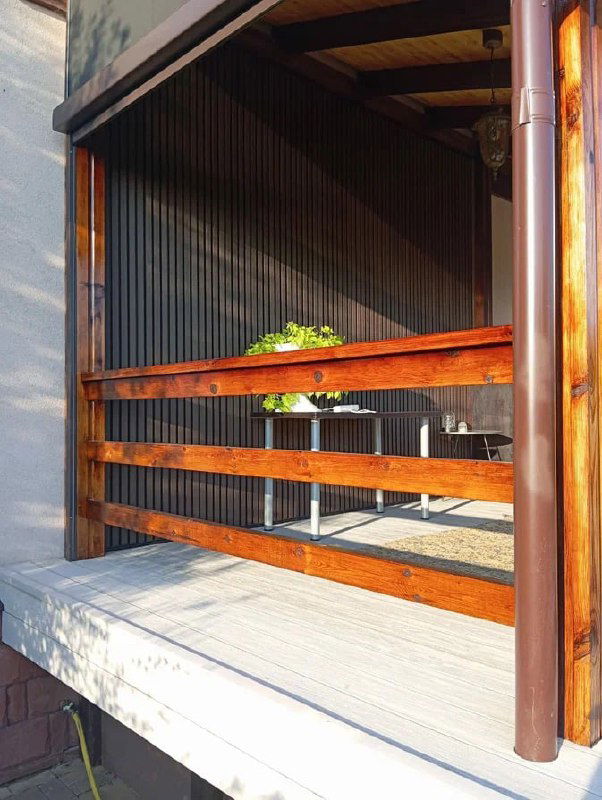 Вид террасы с перилами и тёмными брусковыми панелями ДПК, ракурс подчёркивает сочетание дерева, зелени и светлого покрытия пола для комфортного отдыха.