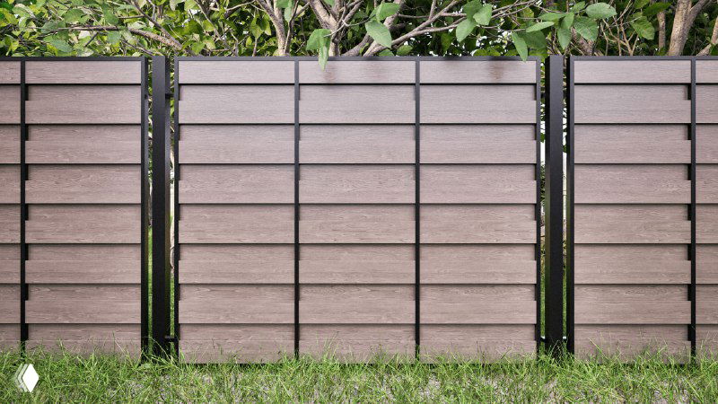 Крупный план секции заборной системы из ДПК с ровными светло‑коричневыми планками и чёрными вертикальными стойками на фоне зелёной травы.