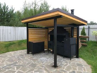 Навес с мангалом и барбекю на каменной площадке в огороженной зоне участка — практичное решение для зоны шашлыков и барбекю.