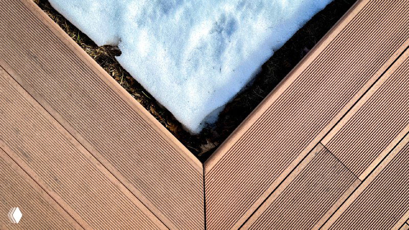 Крупный план углового стыка террасных досок с остатками снега в стыке, демонстрация прилегания панелей и водоотвода.