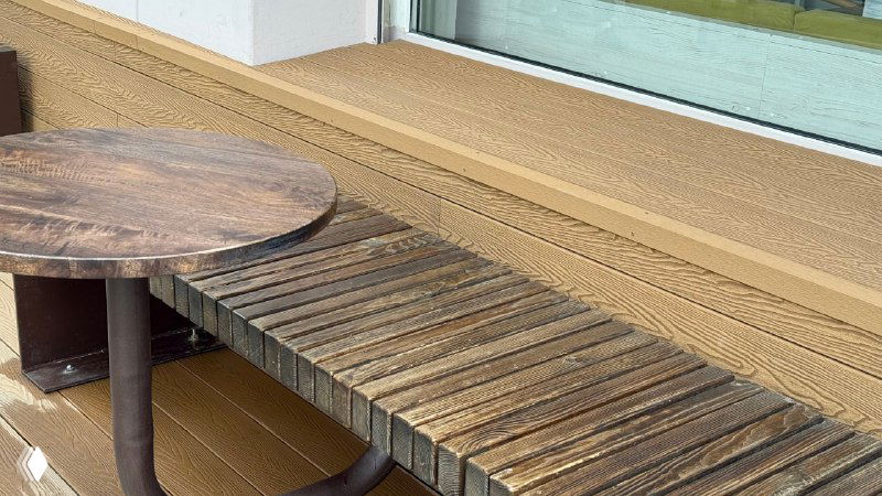 Детальное фото фактуры террасной доски Polivan песочного оттенка и небольшой столик — вид на соединение досок и их текстуру.