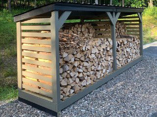 Накрытый дровник с аккуратно сложенными поленьями в деревянной конструкции, практичное хранилище дров на участке дачи.