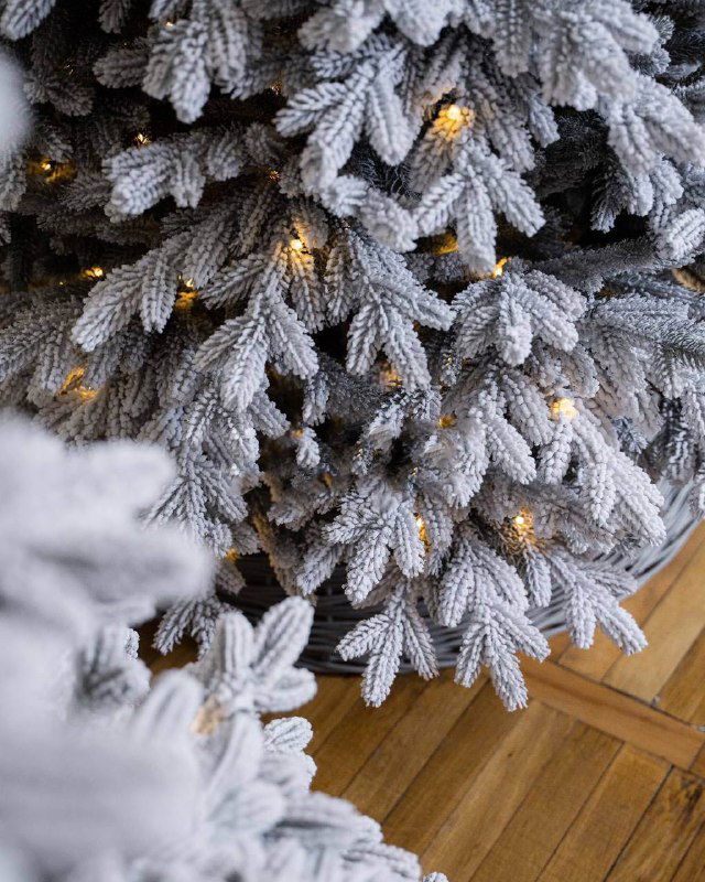 Крупный план заснеженных ПВХ ветвей искусственной ёлки с тёплой встроенной подсветкой — текстура иголок и детали оформления.