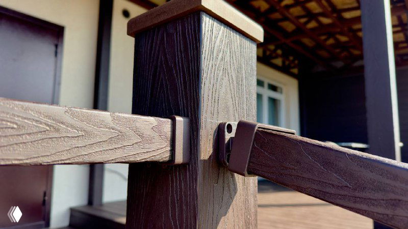 Деталь ограждения и столбика террасы из композитного материала: крепления, рельеф и оттенок коричневого, акцент на фурнитуре и стиле.