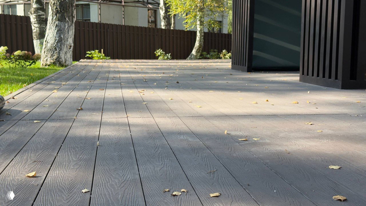 Широкий план террасы из ДПК с берёзами и забором: равномерная укладка досок, рассыпанные листья и перспектива покрытия.