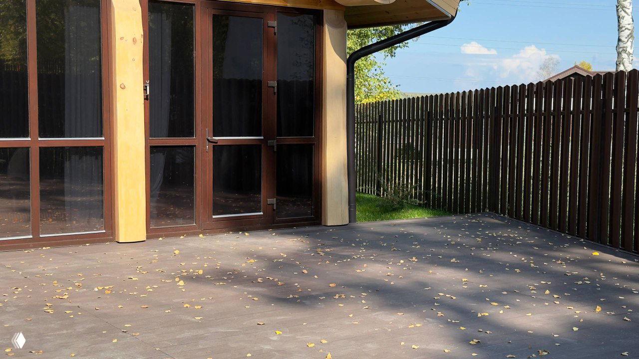 Терраса у входа: ДПК-покрытие перед панорамными окнами, деревянные элементы фасада, опавшие листья и солнечный осенний свет.