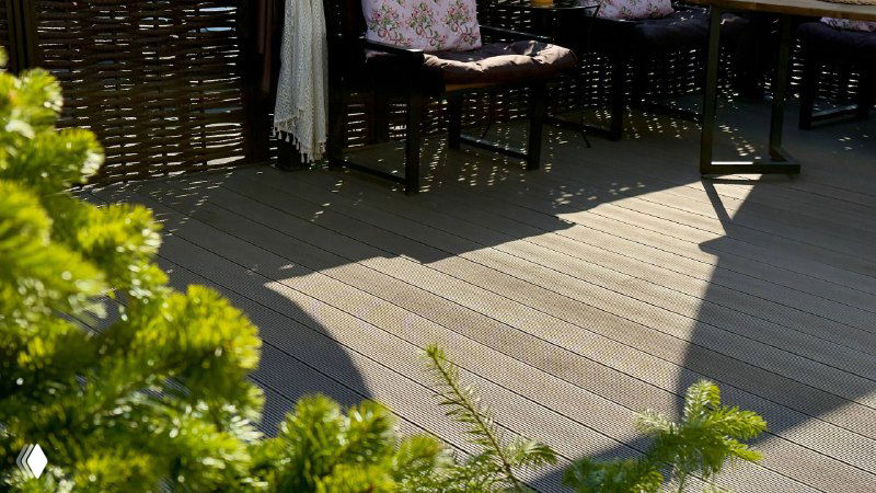 Вид на настил беседки и плетёный забор в солнечных бликах; кадр подчёркивает сочетание зелени, мебели и декоративного ограждения.