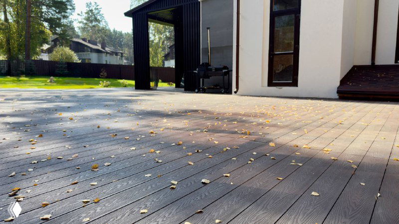 Общий вид террасы у дома: большая площадка из террасной доски, солнечный свет и ограда на заднем плане создают атмосферу участка