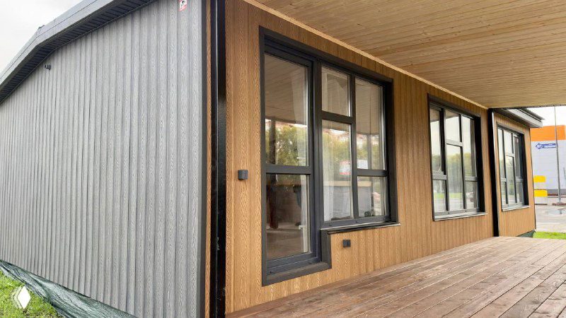 Фасад модульного дома с окнами: сочетание серой и песочной облицовки Polivan SINGARAJA, видна терраса и общий масштаб постройки на выставке.