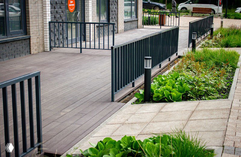 Терраса вдоль фасада с декоративными светильниками и металлическим перилами; настил демонстрирует аккуратную укладку и цветовое решение