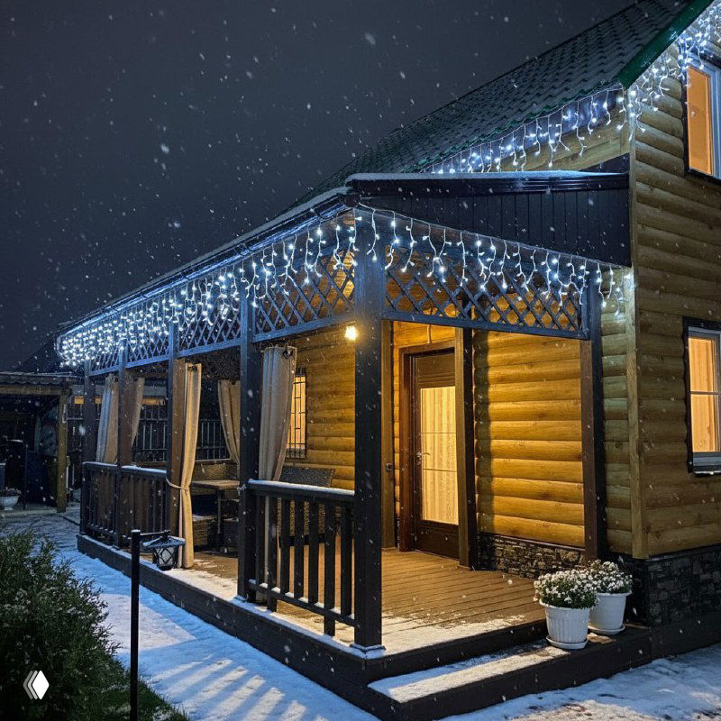 Деревянный дом вечером, карниз и веранда украшены светящейся бахромой; снег ложится на перила и ступени, тёплый свет в окнах