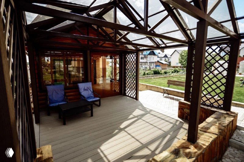 Широкий ракурс крытой террасы с настилом из композитной доски ProDecking, кресла и открывающийся вид на сад, демонстрация готового решения.