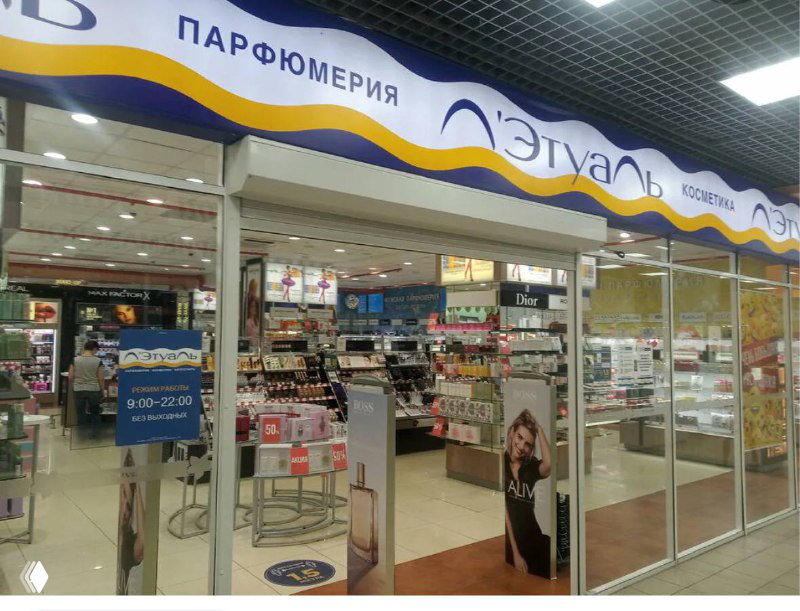 Фасад парфюмерного отдела с витриной и стендом «Л’Этуаль», вид на торговый зал и стойки с косметикой в торговом центре.