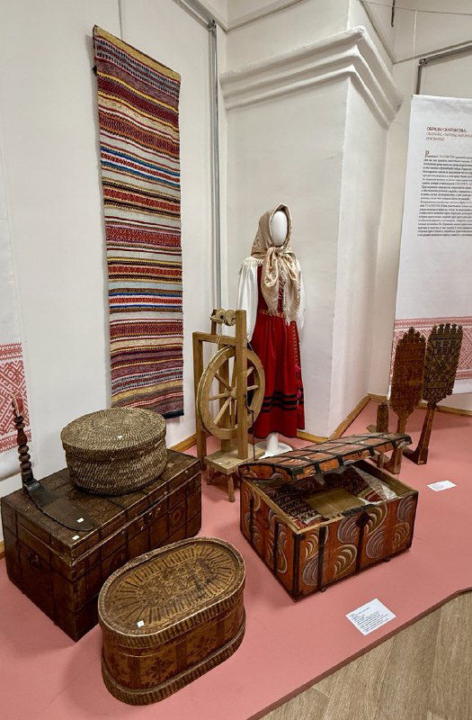 Выставочный уголок с национальными тканями, сундуком и прялкой — предметы народного быта и ремёсел в краеведческой экспозиции.