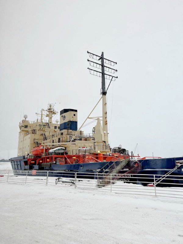 Крупный ледокол у берега в промысленном порту, видна палуба и спасательное оборудование, заснеженная набережная Архангельска