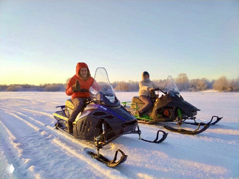 Две снегоходные машины на заснеженном поле, подготовленные для прогулки; на заднем плане видна ровная зимняя равнина и яркое небо