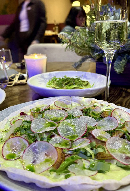 Тонко нарезанные редис и зелёные травы на тонком тесте или салатной основе, крупный план блюда с акцентом на свежесть и подачу ресторана.