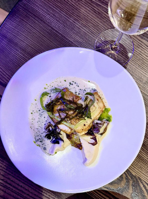 Белая тарелка с аккуратно выложенными грибами и соусом, современная подача горячего блюда в стиле поморско-скандинавской кухни ресторана.