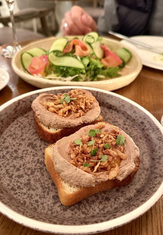 Брускетты с паштетом и хрустящими топпингами на тёмной тарелке, закуска в тёплом свете ресторана, акцент на текстурах и вкусе.