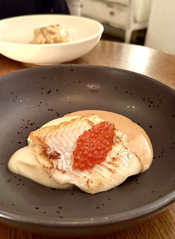 Порция белой рыбы на кремовой подложке с ложкой яркой красной икры сверху — пример местного акцента на рыбе и аккуратной подаче.