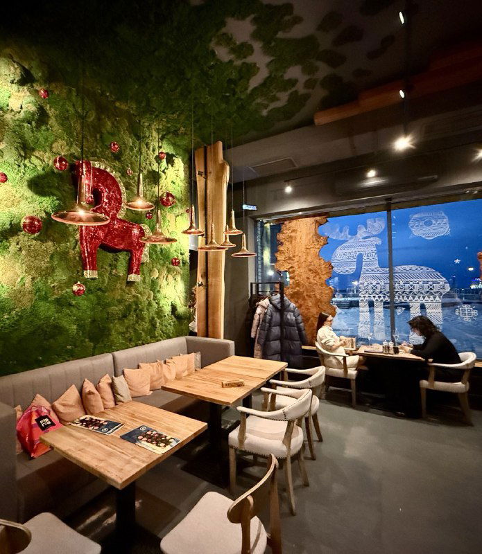 Интерьер ресторана с зелёной текстурной стеной, деревянными столами и дизайнерскими элементами — уютное пространство для ужина в Арханельске.