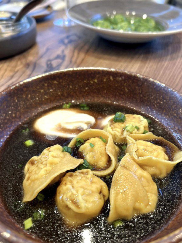 Рыбные пельмени или пельмени в тёмном бульоне на глубокой тарелке — традиционное северное блюдо в современной ресторанной подаче.