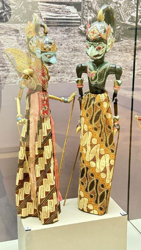 Пара деревянных марионеток с тонкой резьбой и яркими узорами, выставленные в витрине как пример традиционного театра Юго‑Восточной Азии.